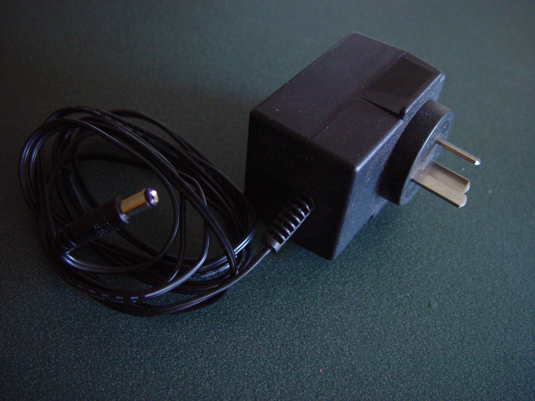 An older plug-in power adapter with an Australian Type I mains plug and barrel connector on a dark surface.
