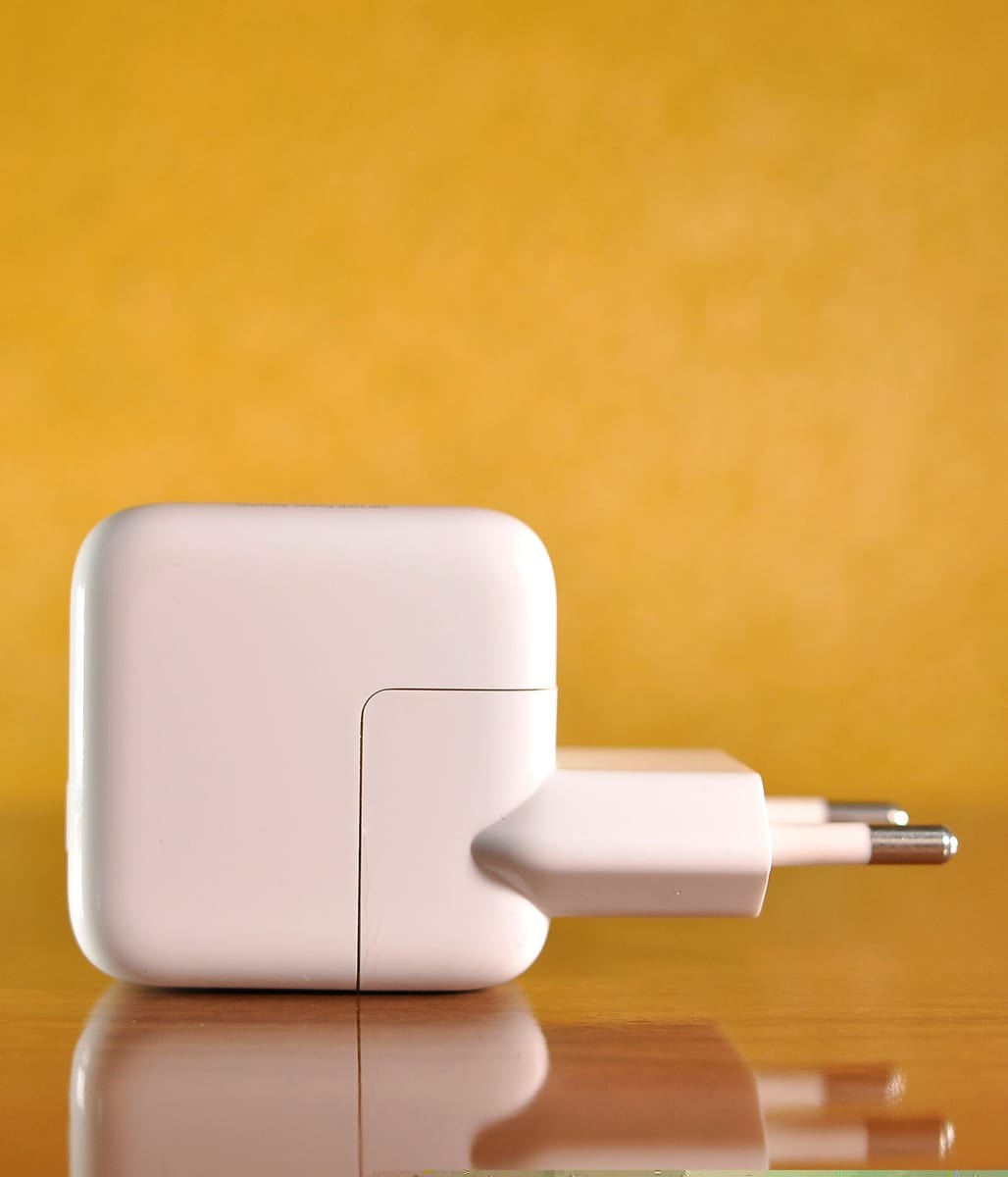 Unmarked white wall adapter photographed on a yellow background as an editorial illustration for California model-record checks.