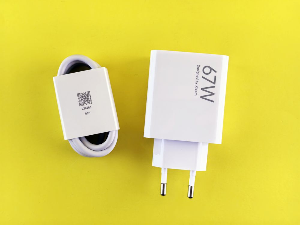 A Xiaomi-branded 67W wall charger and cable photographed against a yellow background.