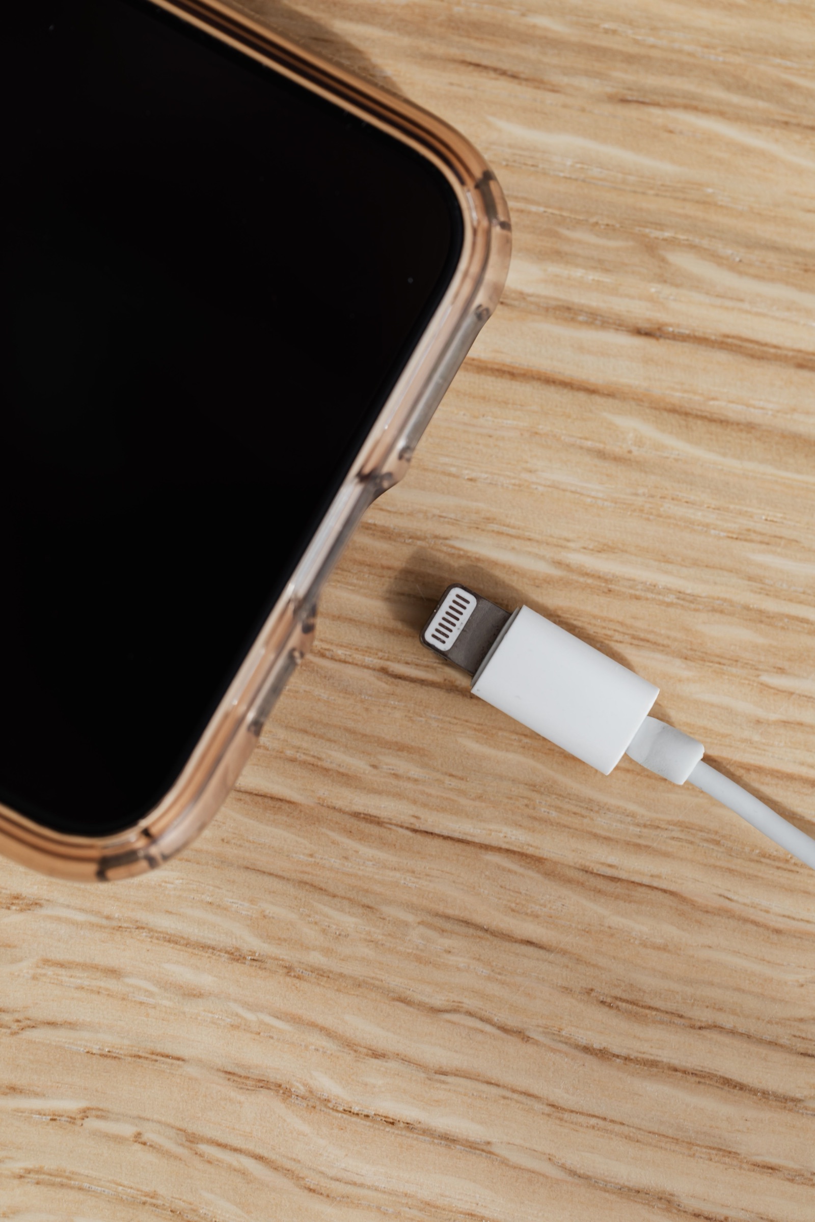 A smartphone beside a disconnected charging cable on a wooden desk, used as an editorial image for connected-hardware cybersecurity reporting.