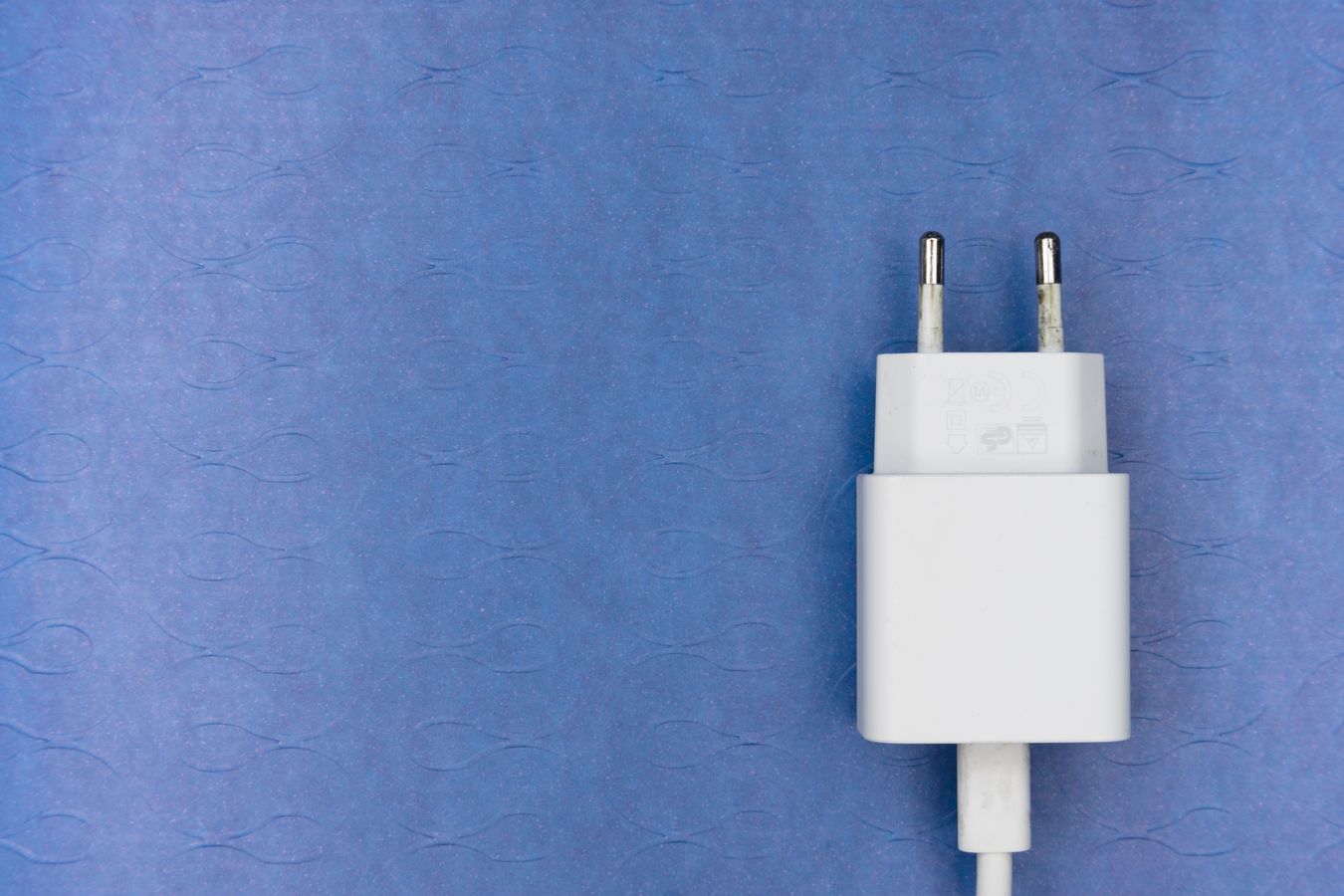 White European two-pin power adapter on a blue surface used as an editorial illustration for CE document checks.