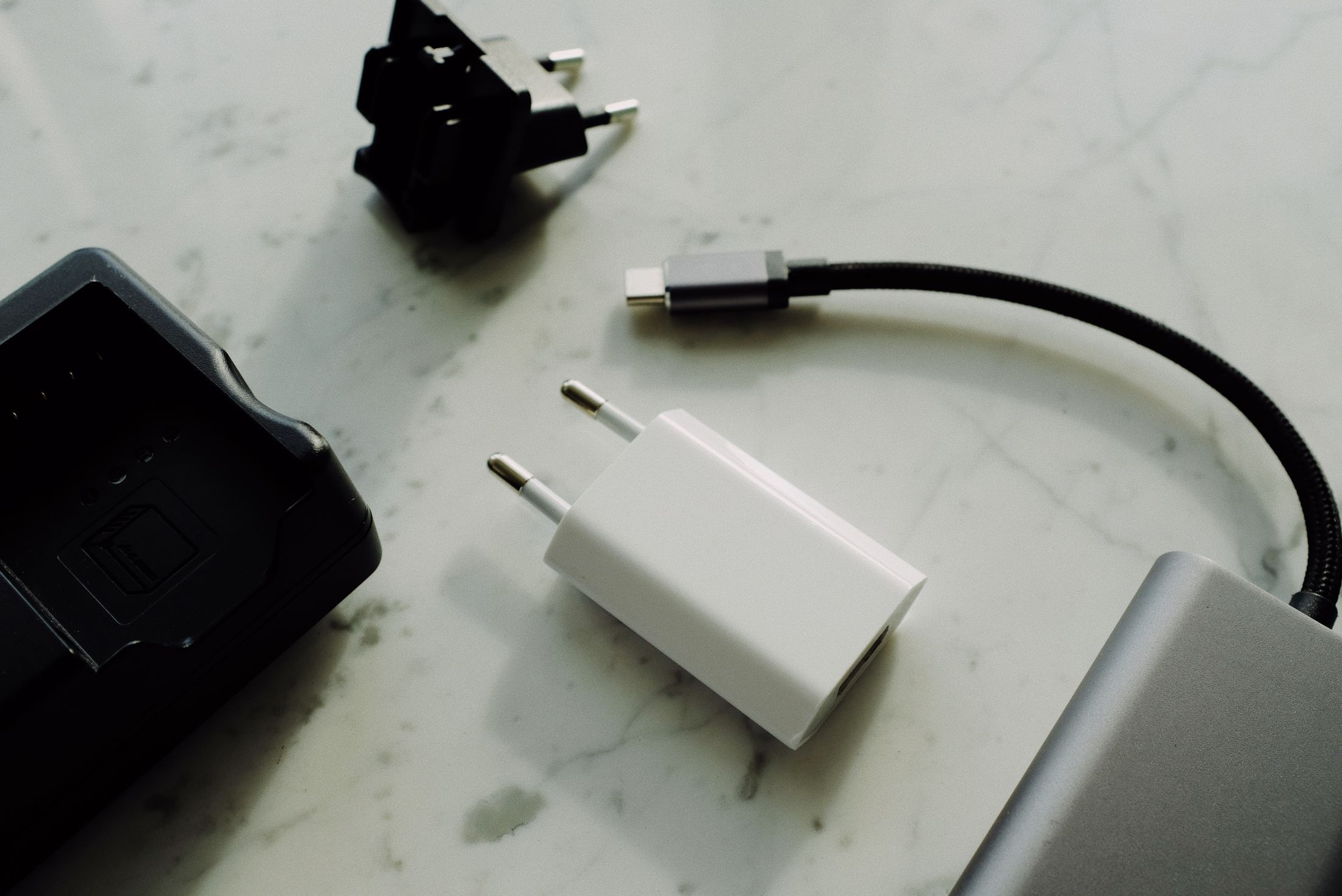 Flat-lay photograph of a white EU-plug charger, USB-C cable, power bank and other charging accessories on a pale marble surface.
