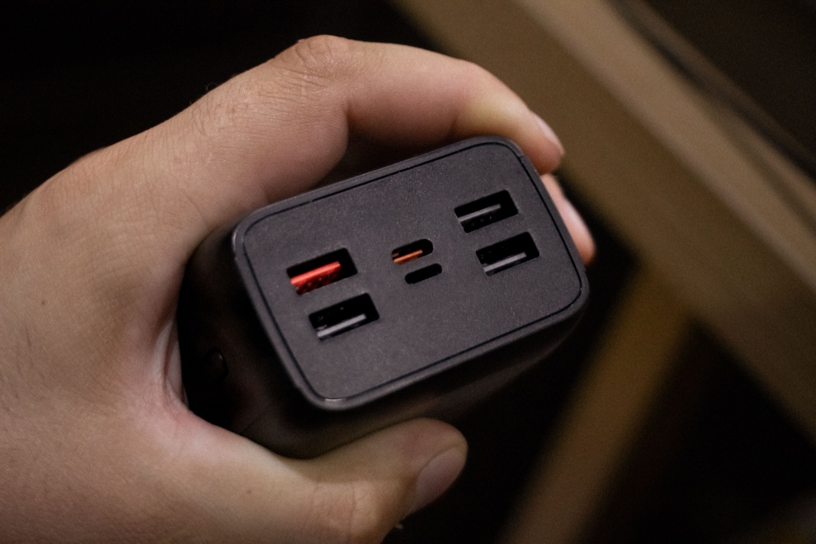 A hand holding a dark multi-port USB power adapter, photographed close-up.