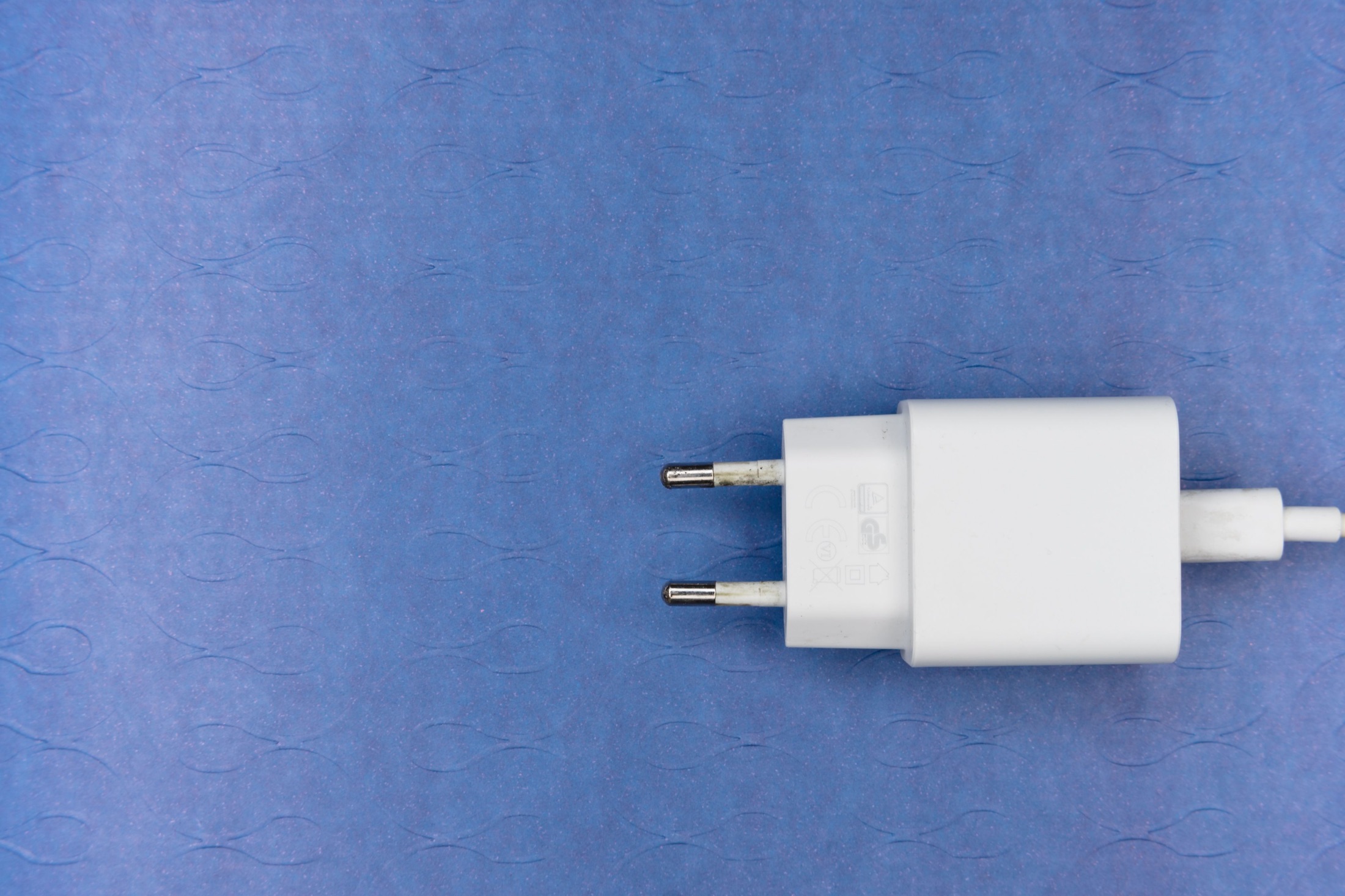 A white two-pin power adapter and cable resting on a textured blue surface.