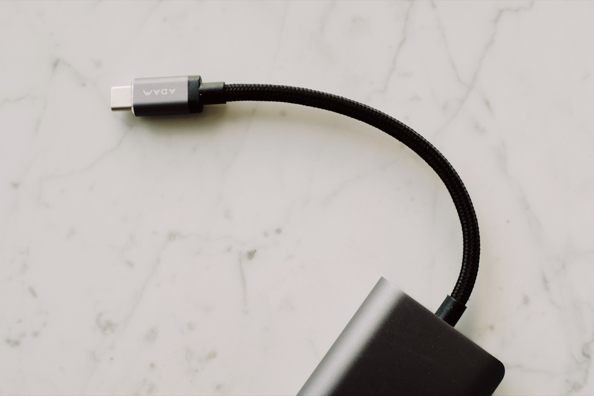 A black braided USB-C cable and adapter on a pale marble surface.